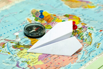 Fototapeta na wymiar travel concept compass and paper airplane on the world map, the buttons mark the places of travel