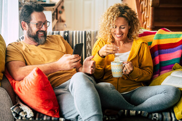 Cheerful young adult couple at home enjoy breakfast morning together drinking tea and looking at...