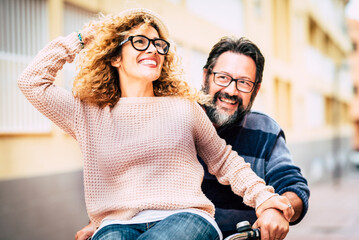 Happy adult mature beautiful couple enjoy and have fun riding a bike together - man carrying woman and laughing a lot - happy active people in leisure time - middle age and eyeglasses portrait