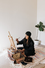 Filipino woman painting on easel while sitting on floor