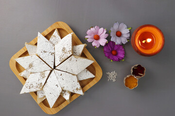 Kaju Katli is a traditional Indian Diamond shaped sweet or Mithai made using cashew paste, sugar, and mava or Khoya. served in a wooden plate over dark background. cashew barfi. Copy space