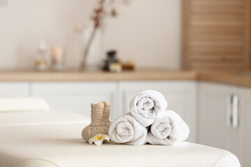 Fototapeta na wymiar Towels with herbal bags and flower on couch in spa salon