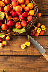 many small apples are lying in a wicker brown basket on a wooden table. several apples are cut in half with a knife with a wooden handle