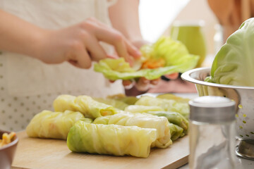 Woman preparing tasty stuffed cabbage rolls on table in kitchen, closeup