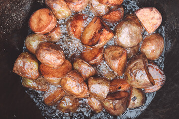 Baked potatoes cooked in yard cauldron with firewood burning in it, with lots of boiling sunflower oil