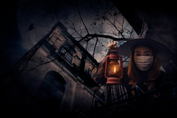 Halloween witch wearing medical face mask holding ancient lamp standing over grunge castle, dead tree, bird fly, full moon and spooky cloudy sky, Halloween and coronavirus or covid-19 concept