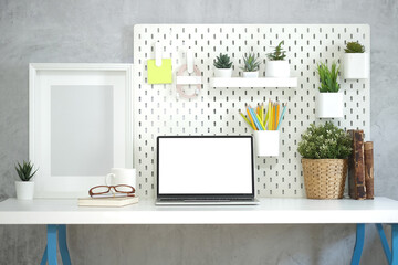 Front view laptop computer with blank screen, empty picture frame and houseplant on white desk.