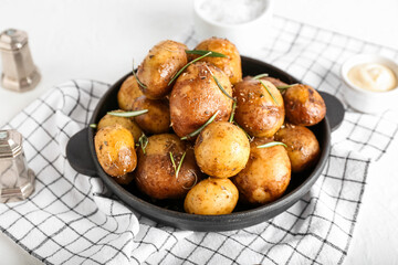 Frying pan with baked potatoes and rosemary on light background