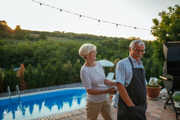 Senior man getting ready for barbecuing. His wife is helping him tying apron