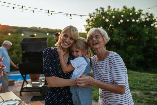 Portrait of three female members of family. Child, mother and grandmother hugging together in the backyard