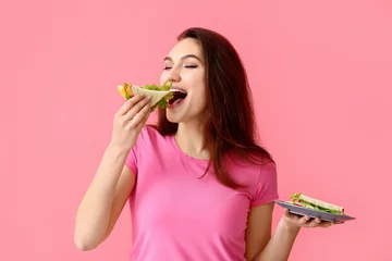 Foto op Plexiglas Young woman eating tasty sandwich on color background © Pixel-Shot