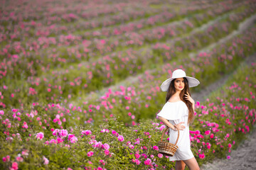 Beautiful young woman portrait in white hat over roses field. Carefree happy brunette with healthy wavy hair having fun outdoor in nature.