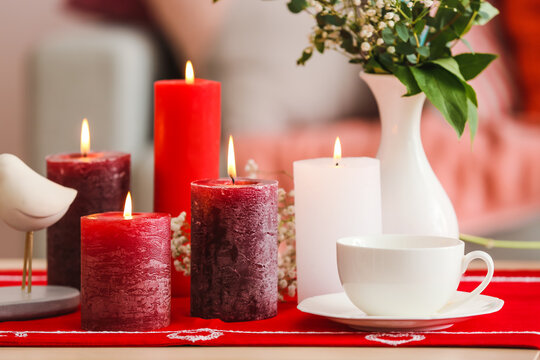 Beautiful burning candles and cup on wooden table in room
