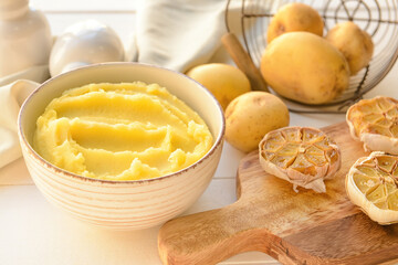 Bowl of tasty mashed potatoes with garlic and vegetables on white wooden background