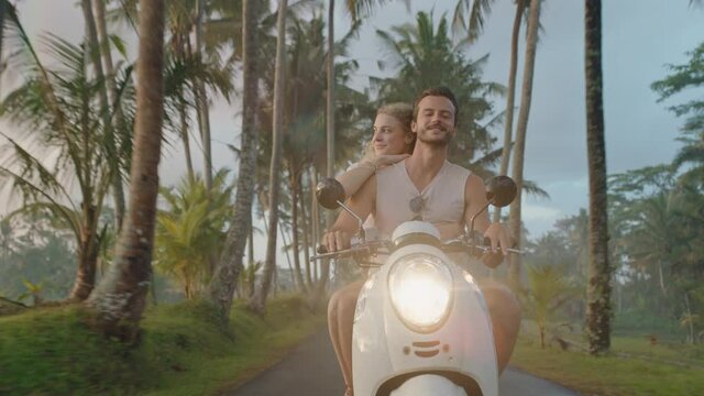 happy couple riding scooter on tropical island happy woman celebrating with arms raised enjoying romantic adventure with boyfriend on motorcycle ride in morning mist