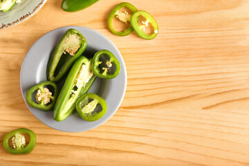 Plate with cut green jalapeno peppers on wooden background