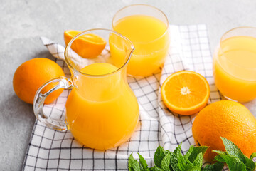 Jug and glasses of tasty orange juice on light background