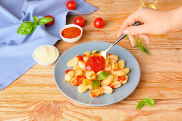 Woman adding tomato sauce to plate with delicious gnocchi on wooden table