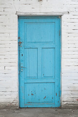 Old shabby blue wooden door on a white brick wall.