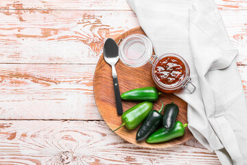 Jar with delicious jam and jalapeno peppers on light wooden background