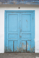 Old shabby blue wooden doors on a white brick wall.