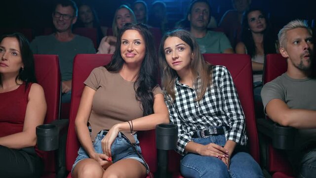 Two female friends gossiping discussing scene actors of film premiere sitting on armchair at cinema