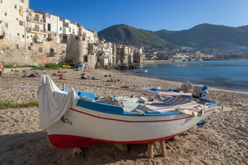 Fototapeta na wymiar Cefalù, Palermo. Spiaggia con barca da pesca sullo sfondo della cittadina.