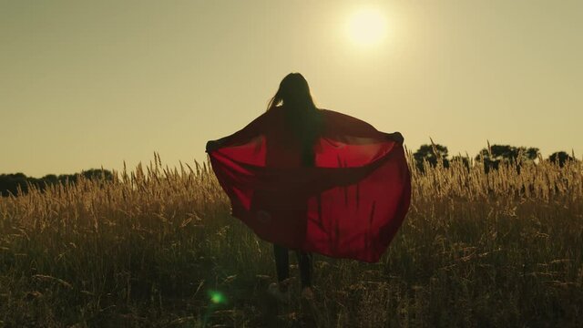 happy girl play superheroes they run across green field in red cloak, cloak flutters in wind. children's games and dreams. Slow motion. teenager dreams of becoming superhero. young girls in red cloak