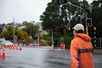 Man wearing face mask walking across the street at intersection. Roadwork traffic cones along the road.