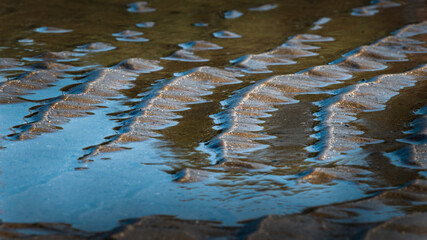 Sand patterns and blue sea water at low tide on the beach