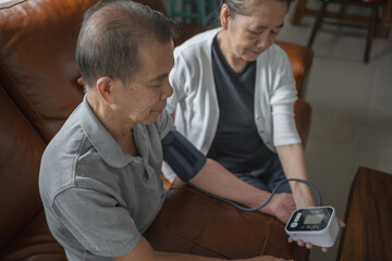 Obraz premium Asian senior couple checking blood pressure at home, they're staring the blood pressure gauge waiting for the result.