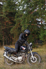 Fototapeta na wymiar biker girl in black clothes and black helmet on a motorcycle