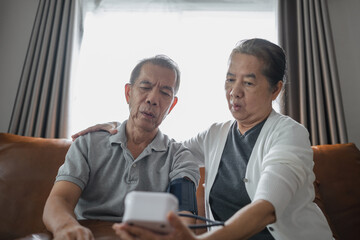 Asian senior couple checking blood pressure at home, after the blood pressure gauge shows the result they shocked.