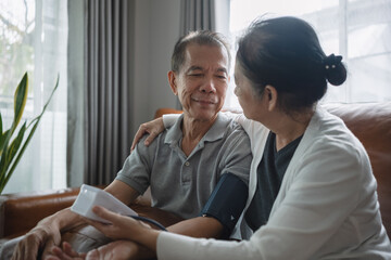 A close-up shot of an Asian senior couple checking blood pressure at home, after the blood pressure gauge shows the result they look at each other and smile.