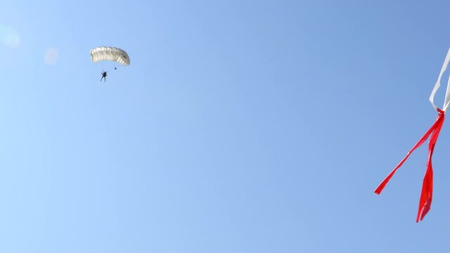 Parachutist with an open parachute is flying and slows down for landing on ground. Skydiving, gliding, parachute jump. Red and white tape indicator shows wind direction
