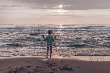 Toddler boy playing by the sea at sunset. Family vacation and lifestyle concept.
