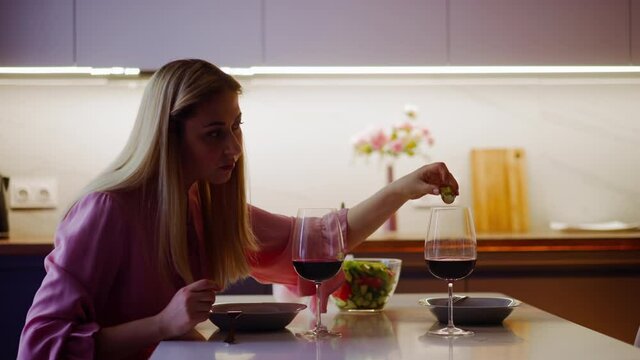 Suspicious blonde woman adds poisonous powder into guest red wine looking back at served romantic date in kitchen at home slow motion