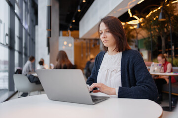 sad business woman with dark short hair working at the computer and bored, work in an office or at home, co-working or public place in a coffee shop. work at a laptop, monotonous and boring activities