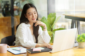 Happy female accountant manager working on laptop in co-working space at cafe