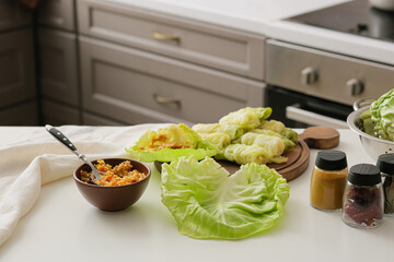 Wooden board with raw stuffed cabbage rolls and ingredients on table in kitchen