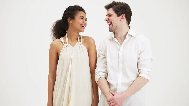 Pleased couple man and woman laughing to the camera standing isolated over white background in the studio
