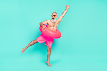 Photo of champion old man raise fist rejoice wear inflatable circle sunglass shorts isolated teal color background
