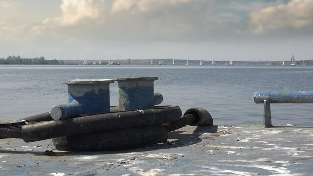 Mooring bollards on an iron pier against backdrop of the open water of river or sea with sails of sports yachts on horizon