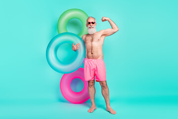 Photo of sportive bodybuilder man hold inflatable circle show biceps wear sunglass shorts isolated...