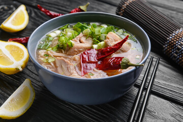 Tasty Chinese soup with chicken in bowl on dark wooden background