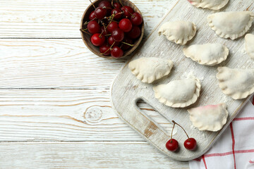 Concept of cooking pierogi with cherry on white wooden table