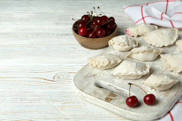 Concept of cooking pierogi with cherry on white wooden table