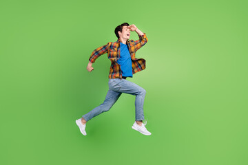 Full size profile photo of funny brunet millennial guy jump wear shirt jeans sneakers isolated on green background