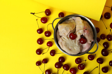 Pot with pierogi with cherry on yellow background