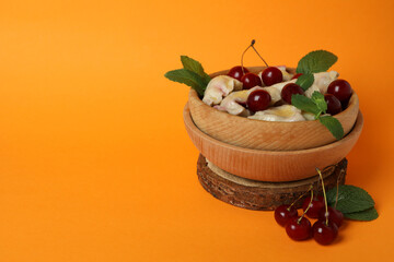 Wooden bowl with pierogi with cherry on orange background